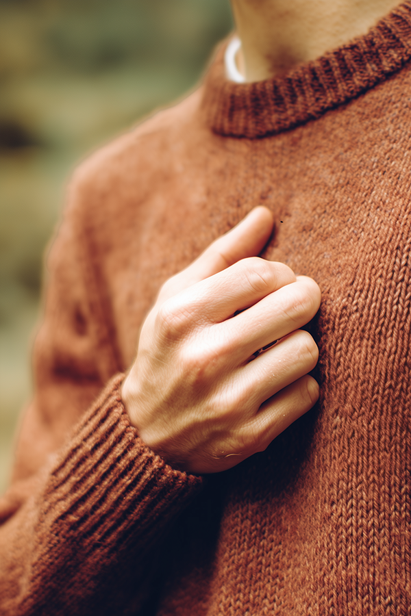 close up of man in burnt orange sweater with softly closed hand held over his heart